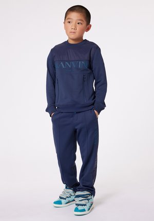 Chándal azul marino con bolsillos con cremallera, con la marca "Lanvin Paris" en el pecho. El conjunto presenta un diseño estructurado con pantalones a juego en azul marino.