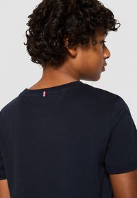 T-shirt in cotone blu navy con collo a giro, maniche corte e una piccola accentuazione rossa e bianca sul collo posteriore. Texture liscia.