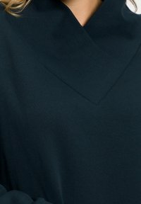 Mörkblå tröja med ribbad V-halsringning och slät textur, i ett mjukt tyg som hänger bekvämt över kroppen.