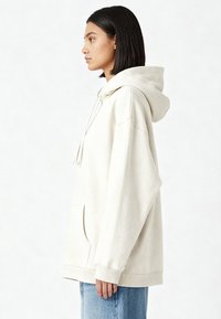 Sweat à capuche surdimensionné beige clair en tissu doux, avec poche kangourou, capuche à cordon de serrage et poignets côtelés.