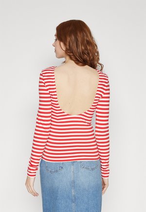 Maglietta a maniche lunghe a righe rosse e bianche con scollatura profonda sul retro, abbinata a una gonna in denim. Il tessuto appare morbido e dalla texture liscia.