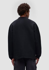 Schwarzer, übergroßer Sweatshirt mit strukturierter Oberfläche, ausgestattet mit einem klassischen Kragen und überschnittenen Schultern. Die Rückansicht zeigt minimale Details.