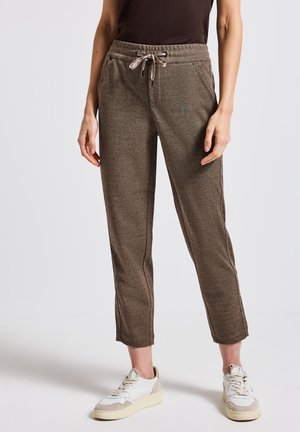 Pantalons joggers marron texturé avec taille à cordon et coutures latérales. Portés avec des baskets blanches et beiges.