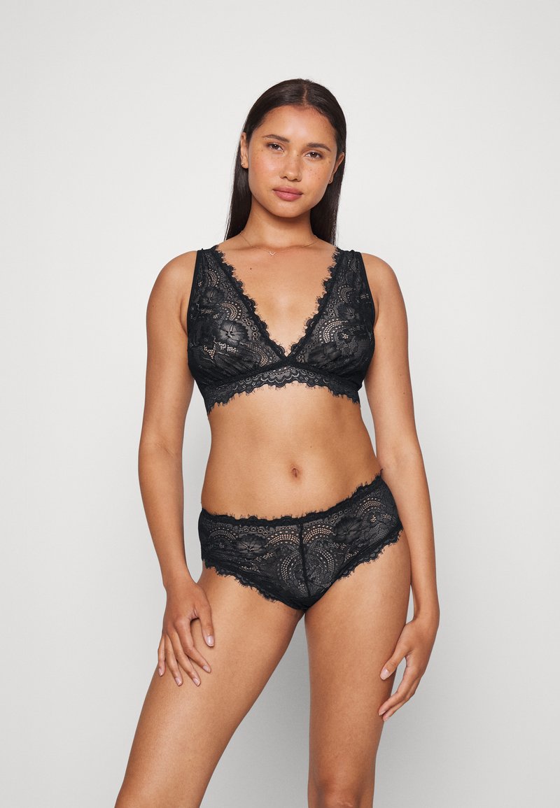 Czarny koronkowy stanik braletka z głębokim dekoltem w kształcie V, falbaniastymi brzegami i pasującymi koronkowymi figami z misternymi wzorami i falbaniastymi wykończeniami.