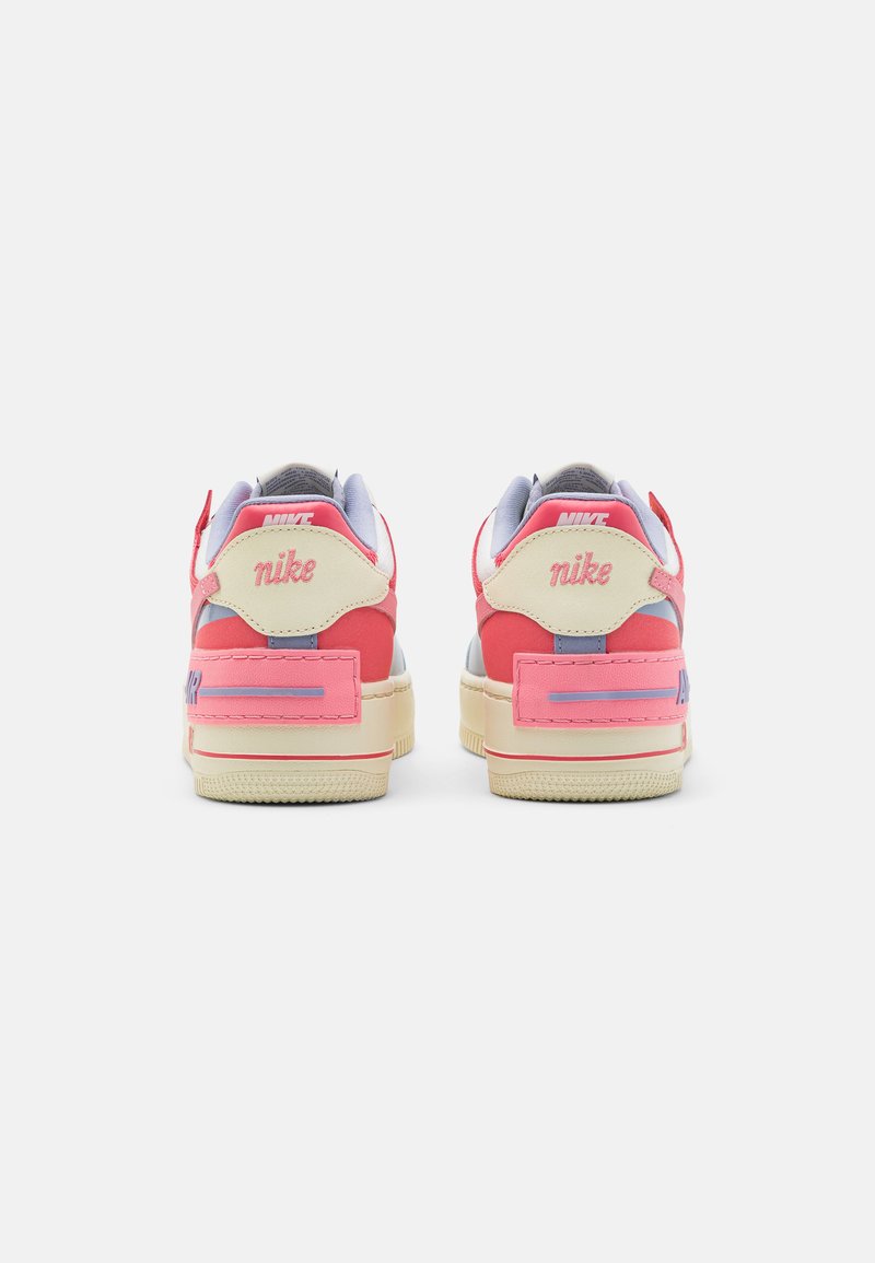 Różowo-kremowe tenisówki Nike z amortyzowaną podeszwą, teksturowanymi materiałami oraz logotypem na pięcie i boku w kontrastowych kolorach.