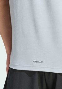 Camiseta deportiva de color azul claro con tela texturizada y dobladillo recto, que presenta el logo "AEROREADY" en negro en la parte inferior.