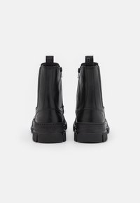 Musta nahkasaappaat nilkkamallia, joissa on sileä pinta, pehmustettu kaulus, sivuvetoketjut ja teksturoitu kumipohja. Logo-yksityskohta kantapäässä.