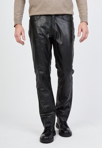 Schwarze Lederhosen mit glatter Textur, schlanker Passform und Taschen; kombiniert mit schwarzen Schnürschuhen und einem hellbeigen Pullover.