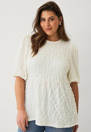 Weiße strukturierte Bluse mit Puffärmeln, rundem Ausschnitt und gerafftem Taillenbund. Kombiniert mit Jeans.