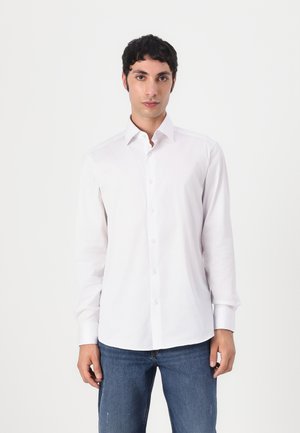 Camisa blanca de manga larga con cuello abotonado, hecha de tela suave; presenta una tapeta de botones en el frente y un diseño ajustado.