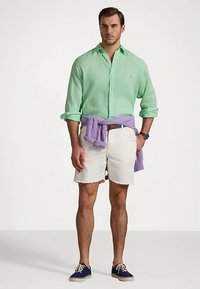 Ανοιχτό πράσινο πουκάμισο λίνου, άσπρο ξεφτισμένο σορτς, μοβ πουλόβερ δεμένο στη μέση και σκούρα μπλε αθλητικά παπούτσια. Καθημερινό καλοκαιρινό ντύσιμο.