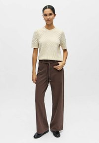 Haut en maille crème à manches courtes avec un motif texturé, associé à un pantalon large marron et à des chaussures plates noires. Coupe simple et décontractée.