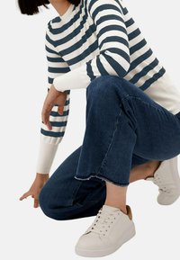 Maglione a righe bianche e blu notte, con polsini aderenti, abbinato a jeans cropped blu scuro con orlo sfilacciato, completato da sneakers bianche con dettagli marroni.