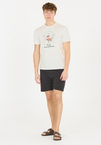 Ljusbeige t-shirt med en grafisk design av en flamingo, i kombination med svarta shorts och bruna justerbara sandaler för avslappnad klädsel.