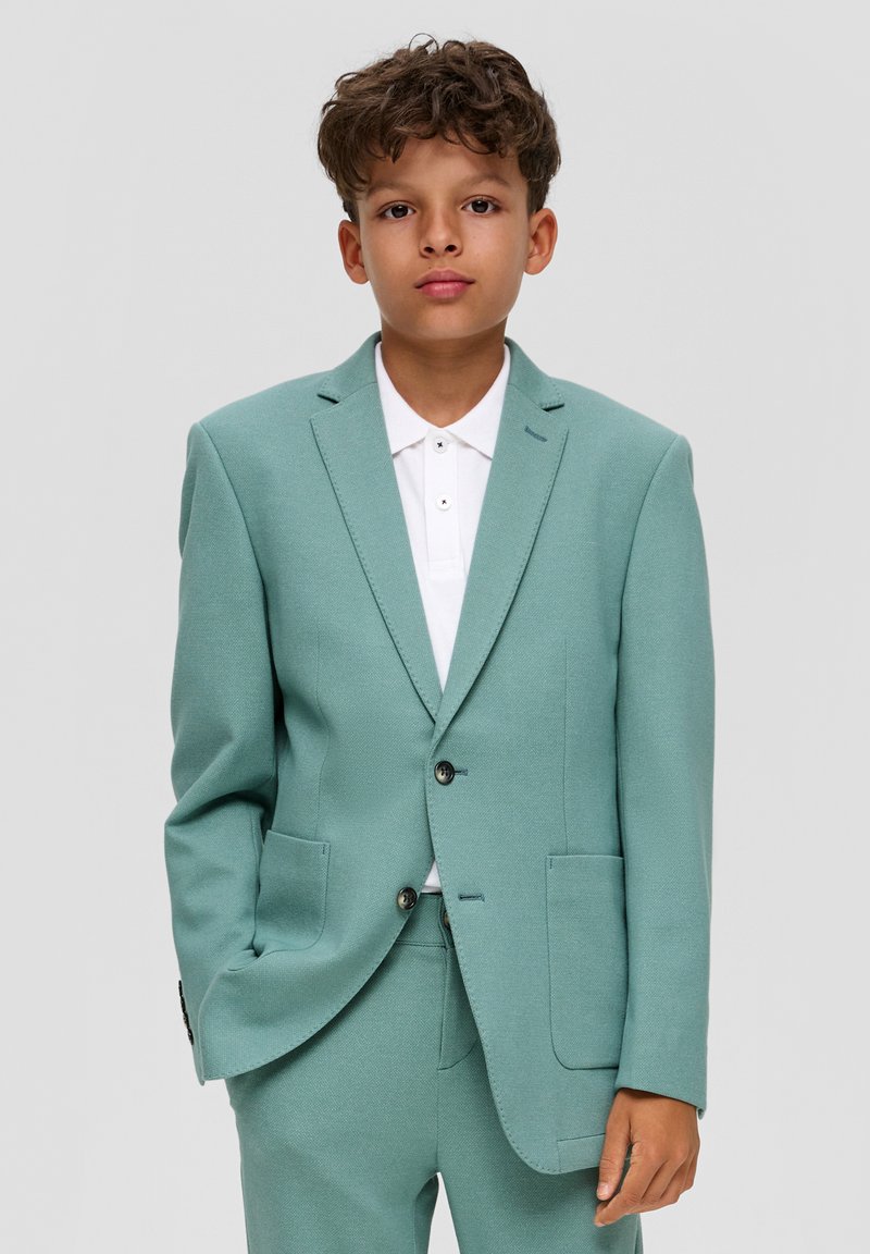 Jasnoniebieski garnitur z teksturowanym wykończeniem, jednorzędowa marynarka, dwie kieszenie z przodu oraz biała koszula z kołnierzykiem pod spodem.