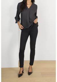 Černá blůza s dlouhým rukávem a výstřihem do V s texturovaným designem. Spárována s přiléhavými černými džíny a lodičkami s špičatou špičkou, které mají ozdobný přezku.