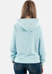 Sudadera azul claro con capucha ajustable, puños y dobladillo acanalados, textura suave y corte relajado, combinada con jeans de mezclilla oscura.