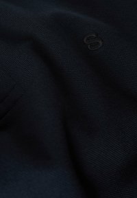 Tejido de punto azul marino con un patrón texturizado y un logo en relieve. El material es suave y ligeramente elástico.