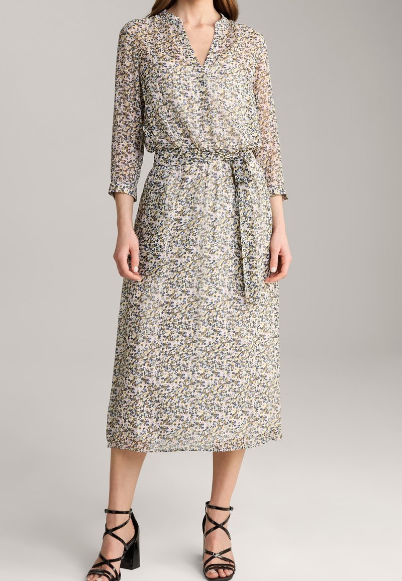 Sukienka w kwiaty, lekka, z dekoltem w kształcie litery V, rękawami 3/4, paskiem w talii i długości midi. Na materiału znajdują się różnorodne, małe kolorowe wzory kwiatowe.