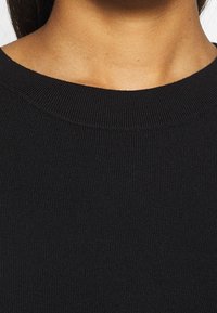 Zwarte gebreide trui met een geribbelde textuur en een ronde hals. De stof lijkt zacht en elastisch zonder zichtbare patronen of accenten.