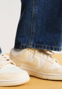 Bež Nike tenisice s antilop i kožnim teksturama, zaobljenim nosom, perforacijama i vezicama, uparenim s tamnoplavim trapericama.