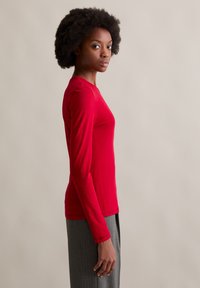 Długo rękawowa koszula w jaskrawym czerwonym kolorze, wykonana z gładkiego materiału. Dopasowany krój z okrągłym dekoltem, widoczne szwy wzdłuż ramion i boków.
