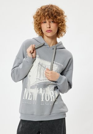 Sudadera con capucha gris que presenta un gráfico blanco del Puente de Brooklyn de Nueva York y texto. Tejido de mezcla de algodón con puños de canalé. Corte casual.