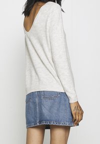 Jasnoszary sweter z niskim tyłem, w połączeniu z niebieską dżinsową mini spódnicą. Sweter ma miękką fakturę i dopasowane rękawy.
