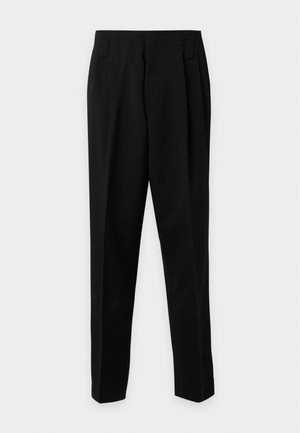 Mand iført en sort dobbeltradet blazer med satin revers, lyserød skjorte, sorte bukser, brune sko og solbriller mod en hvid baggrund.