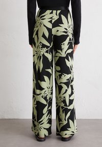 Black wide-leg pants with a green floral pattern, featuring a stretchy waistband and a smooth fabric texture. Worn with a black top.