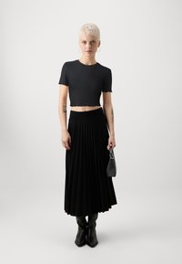 Černý žebrovaný crop top s roztrhaným lemem, v kombinaci s dlouhou plisovanou černou sukní. Doplněno malou černou kabelkou a kozačkami po kolena.