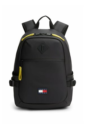 Mochila negra con tiradores de cremallera amarillos, bolsillo delantero con cremallera, correas acolchadas para los hombros y parche con el logo de Tommy Jeans en la parte frontal inferior.