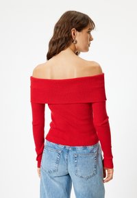 Top rosso a costine, scollato sulla spalle, con maniche lunghe, design aderente e tessuto testurizzato, abbinato a jeans a vita alta blu chiaro.