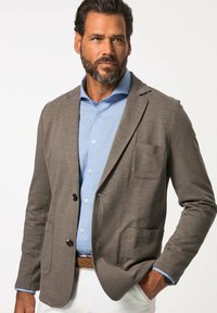 Blazer grigio in tessuto testurizzato, dotato di due tasche frontali, una chiusura a un bottone e indossato sopra una camicia azzurro chiaro.