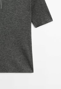 Ciemnoszary prążkowany top z krótkim rękawem z kołnierzem zapinanym na suwak. Tkanina wydaje się miękka z subtelną teksturą. Prosty design, bez dodatkowych akcentów.