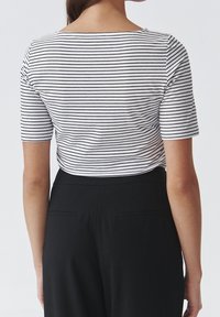 Top de manga corta a rayas en blanco y negro, con escote barco y ajuste ceñido, combinado con pantalones negros de cintura alta.
