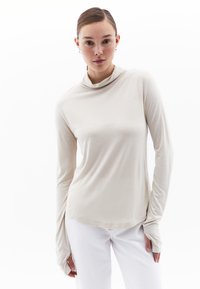 Lange mouwen, crèmekleurige coltrui van zacht, lichtgewicht materiaal met een ontspannen pasvorm. Heeft duimgaten en een gebogen zoom. In combinatie met witte jeans.
