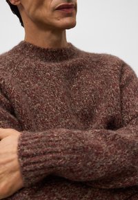 Sweter dzianinowy w głębokim burgundzie z teksturowanym, puszystym wykończeniem. Posiada wysoki dekolt i ściągacze, podkreślające ciepło i wygodę.