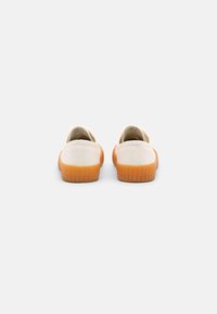 Canvas sneakers in off-white with a textured orange rubber sole. Features stitched detailing at the heel and a smooth finish.