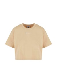 Lyhythihainen, pehmeästä puuvillasta valmistettu beige crop-top, jossa on pyöreä kaula-aukko. Edessä on huomaamaton valkoinen logo.
