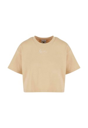 Lyhythihainen, pehmeästä puuvillasta valmistettu beige crop-top, jossa on pyöreä kaula-aukko. Edessä on huomaamaton valkoinen logo.