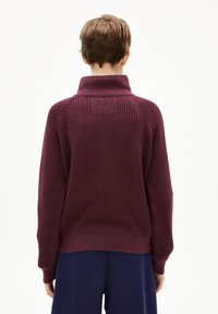Bordeaux geribbelde turtleneck trui met een hoge kraag, drop shoulders en een gemêleerd breipatroon, gecombineerd met marineblauwe broek.