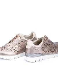 Zapatillas metálicas de color rosa dorado con detalles perforados, acentos suaves en beige, cordones elásticos y una suela blanca gruesa.