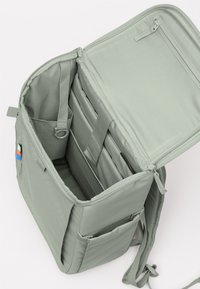 Grau gefärbter Stoffrucksack mit einem durch Reißverschluss verschlossenen Hauptfach, Innenfächern, verstellbaren Riemen und einem kleinen farbigen Logo-Patch.