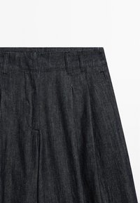 Donkerdenim broek met een vlakke voorkant, ritssluiting en riemlussen. De stof heeft een soepele textuur met een subtiele glans en contrasterende stiksels.
