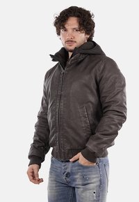 Giacca bomber in pelle marrone con cappuccio, dotata di polsini e orlo a coste, chiusura frontale con zip e dettagli di cucitura discreti.