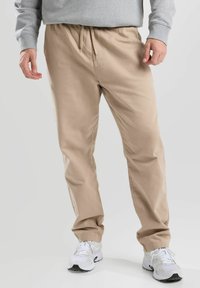 Pantalons beige légers avec une taille élastique et un cordon de serrage. Texture lisse, coupe droite, associés à des chaussures de sport blanches.