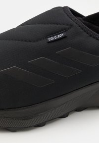 Black slip-on sneaker made of textured material, featuring distinguished black three-stripe design and a "COLD.RDY" label near the opening.