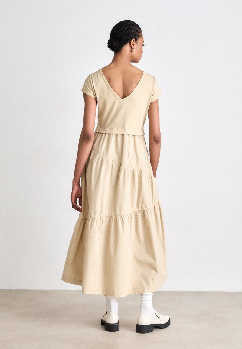 Beige katoenen maxi-jurk met korte mouwen, een V-hals aan de achterkant en gelaagde lagen. Gestyled met witte sokken en crèmekleurige schoenen. Eenvoudig ontwerp.