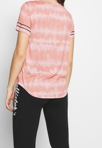 Pink tie-dye t-shirt with short sleeves, featuring dark stripes on the sleeves and a relaxed fit, paired with black leggings.